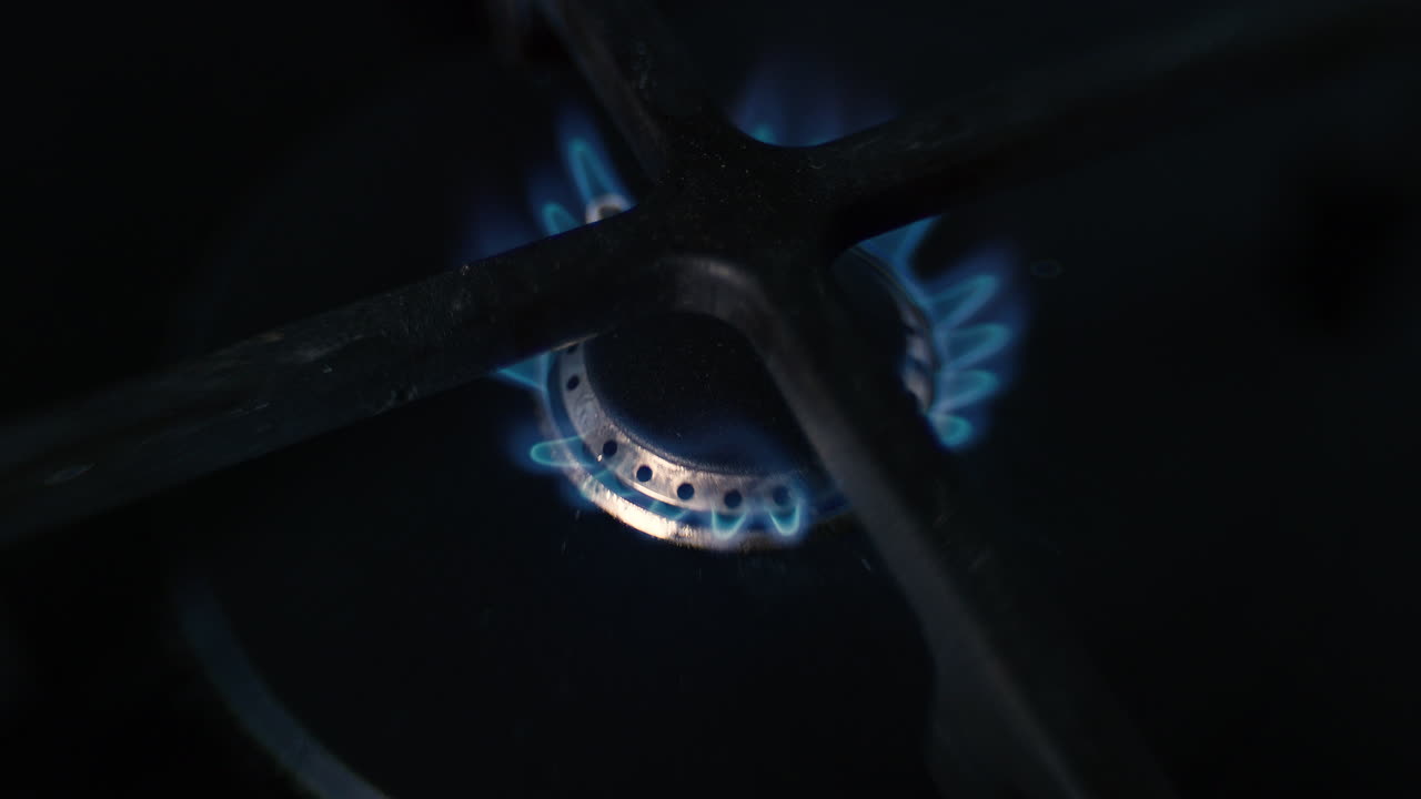A distorted close up of a small hob on a ceramic gas stove being lit, burning for a while and then turning off