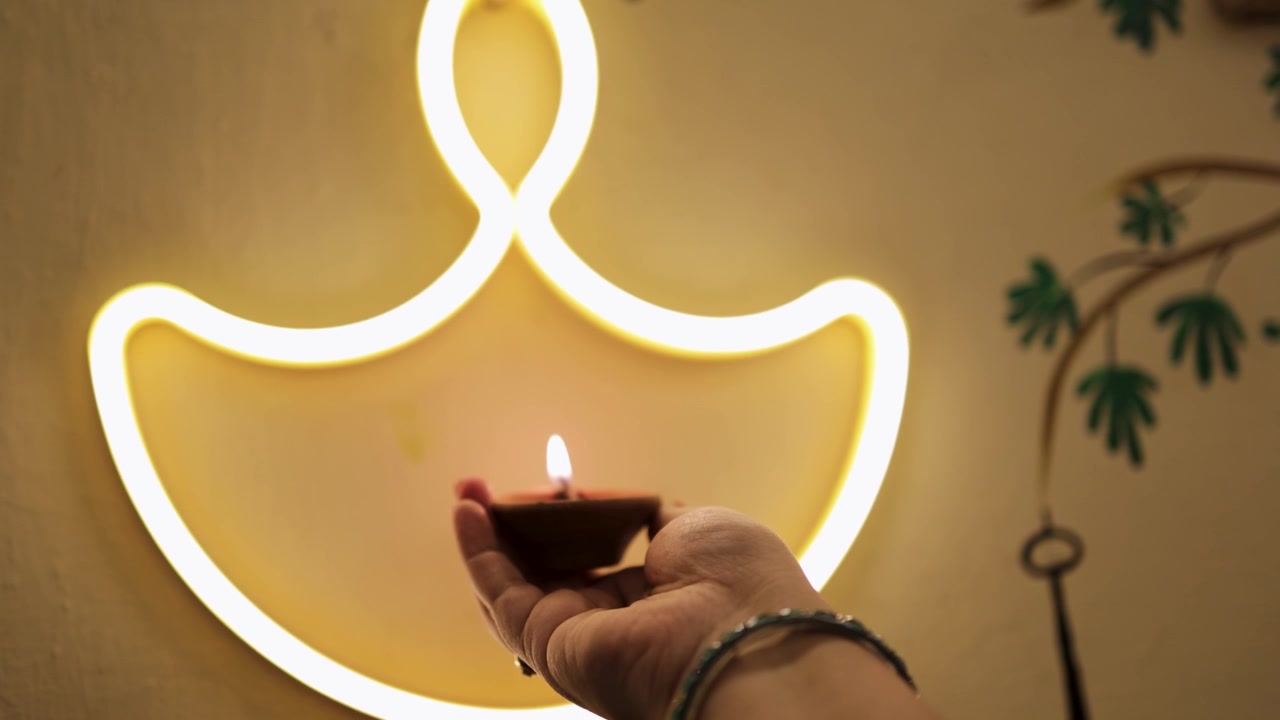 Mano che tiene una tradizionale Diya in argilla davanti a una decorazione luminosa di lampade Diwali