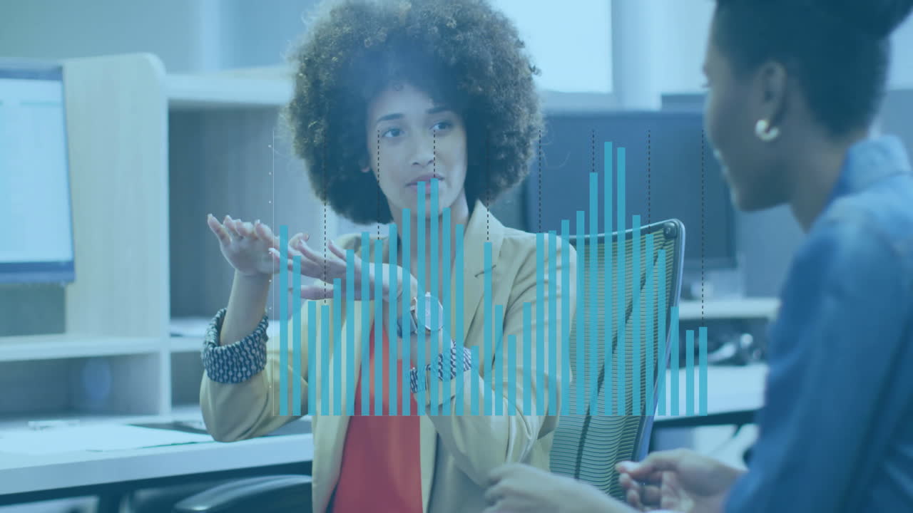 Coworkers discussing business data in cubicle, showing animated blue bar charts over monitors