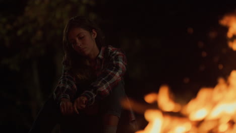 tired woman look bonfire on dark evening. nature explorer sit enjoy camp outside