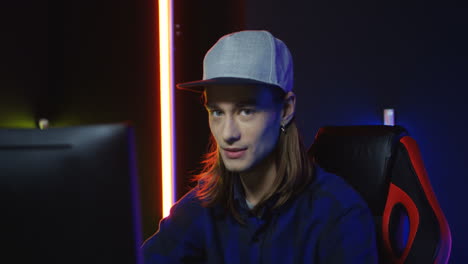 close up view of young serious man wearing cap and playing a game on the computer, then looks at camera and smiles