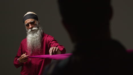 close up low key studio lighting shot of two sikh men folding fabric for turban against plain background