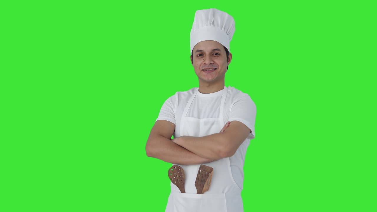 Ritratto di chef professionista indiano felice in piedi a braccia incrociate su green screen