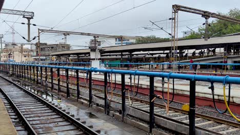 view of vadodara railway station, bustling with people waiting on platform for trains, set against backdrop of a cloudy sky in gujarat, india.