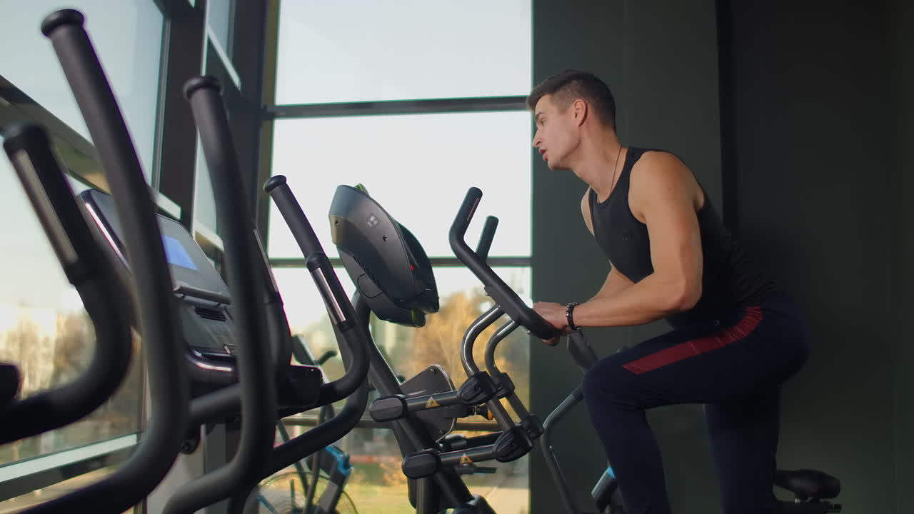 Spor salonunda eliptik bisiklette egzersiz yapan güzel, formda, sportif, pozitif genç adam
