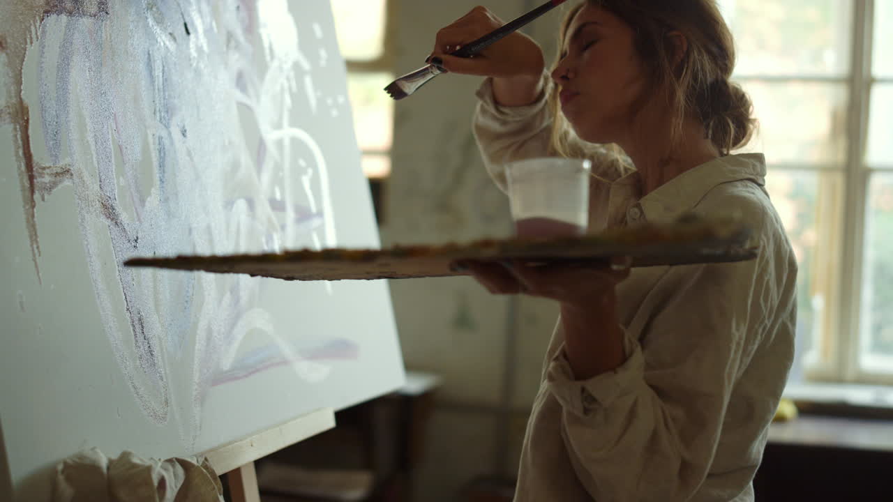 피곤한 화가가 실내에서 이마를  ⁇ 고 창의적인 소녀가 아트 스튜디오에서 그림을 그리고 있습니다.