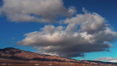 vehicular traffic moving along the highway at the base of the mojave desert mountains with a cloudscape overhead - time lapse