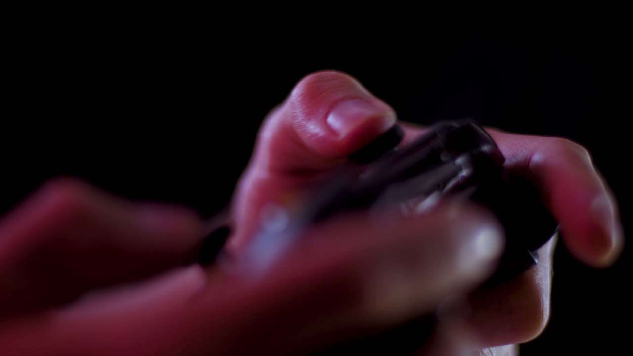 Playing video games in a darkened room with a black background close up on a controller joystick playing quickly soft focus