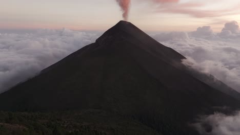 Toma-Aérea-Inclinada-Que-Revela-Un-Volcán-En-Erupción,-Puesta-De-Sol-Muy-Por-Encima-De-Las-Nubes