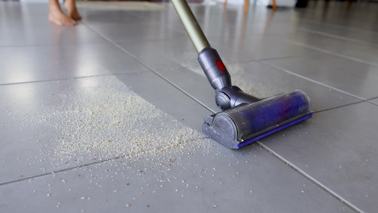 A vacuum cleaner removes crumbs from kitchen tiles in a well-lit home environment, demonstrating effective cleaning techniques
