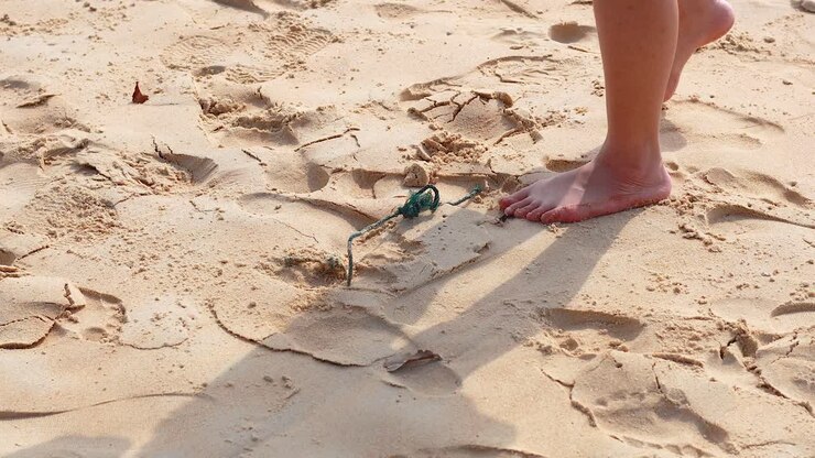 A person picks up a rope from the sand on a sunny beach, showcasing a simple, serene moment