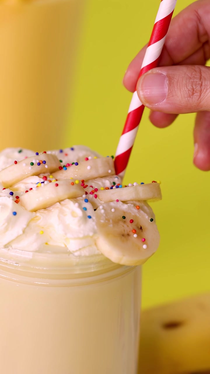 Mano che inserisce una cannuccia a strisce in un frullato di banana con panna montata