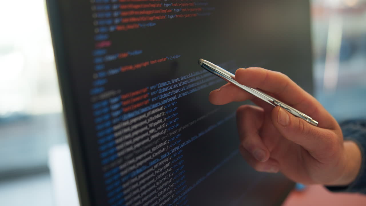 Close-up of Hand with Stylus Reviewing Code on Monitor