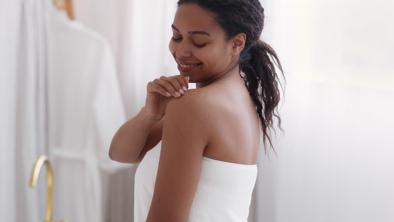 Woman applying lotion to shoulder after bath