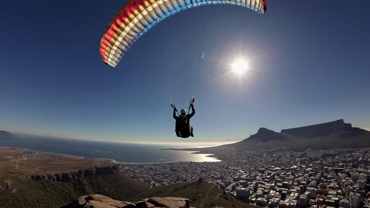 Video aereo che riprende un parapendio che si libra sopra un paesaggio urbano costiero, con una vista grandangolare