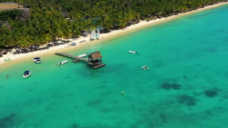 Glide-above-a-sunny-pier-and-crystal-clear-ocean-at-Trou-aux-Biches,-Mauritius