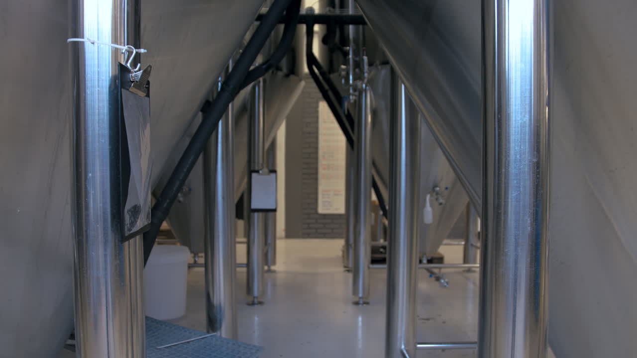 Rack focus change from view between large stainless steel fermentation tanks in a brewery to a wall with a whiteboard full of writing