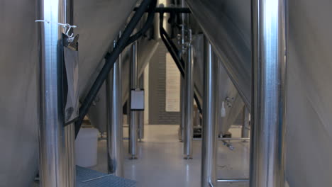rack focus change from view between large stainless steel fermentation tanks in a brewery to a wall with a whiteboard full of writing