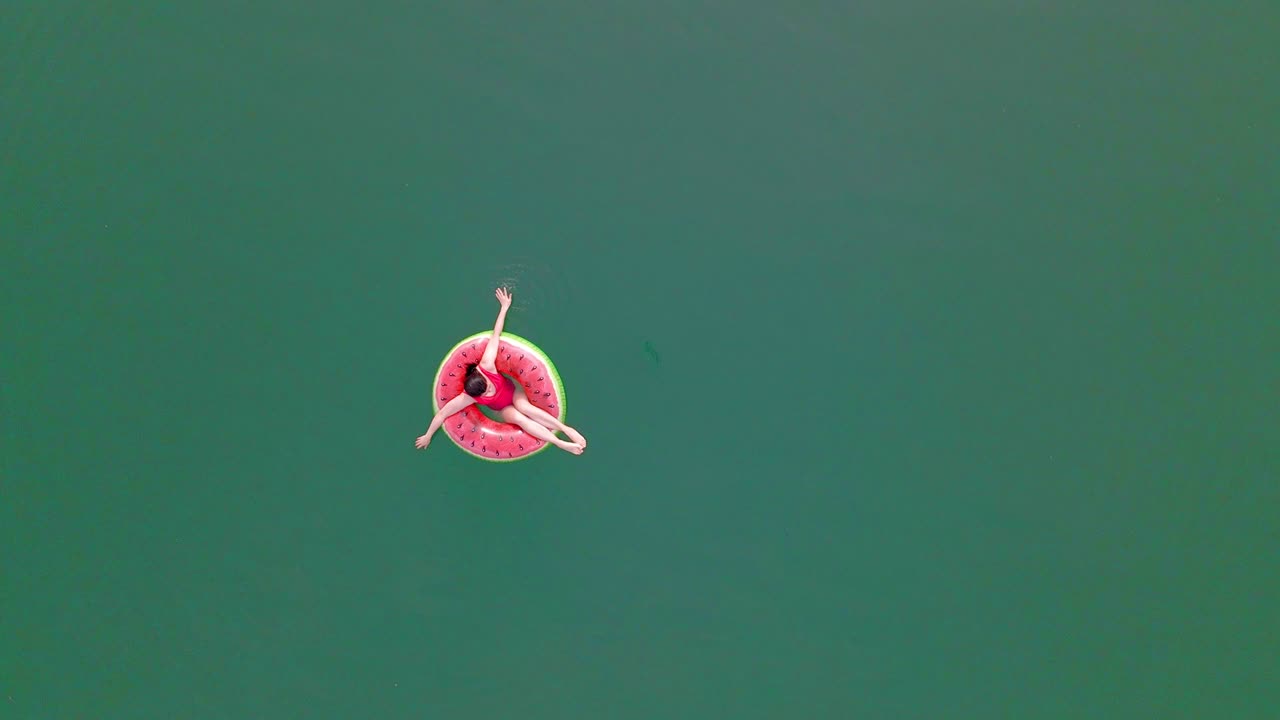 overhead top view of woman swimming with watermelon swimming circle in blue water