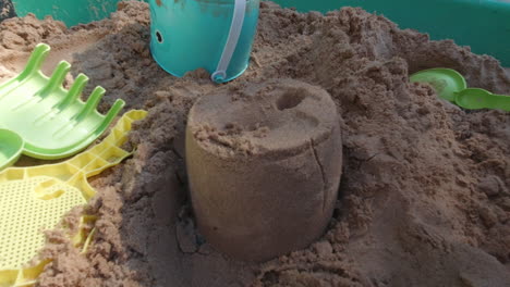 Child-lifting-a-bucket-of-sand-to-revel-a-sand-castle,-shot-in-a-children's-play-sandpit