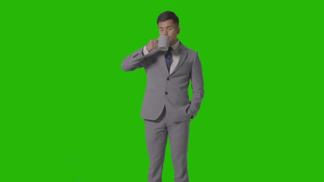 studio shot of businessman in suit holding and drinking cup of hot drink against green screen