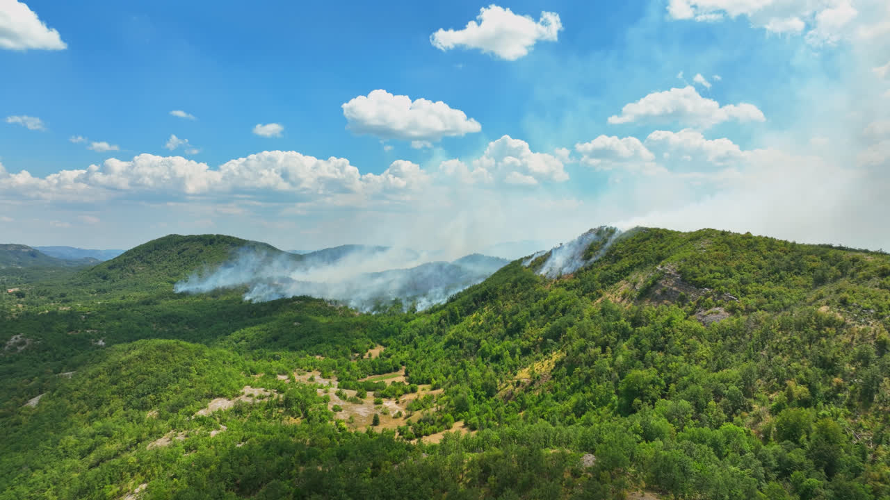 Establishing drone shot of hills on fire, smoke rising from smoldering forest