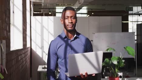 african american businessman holding laptop looking ahead shifting gaze to camera and smiling