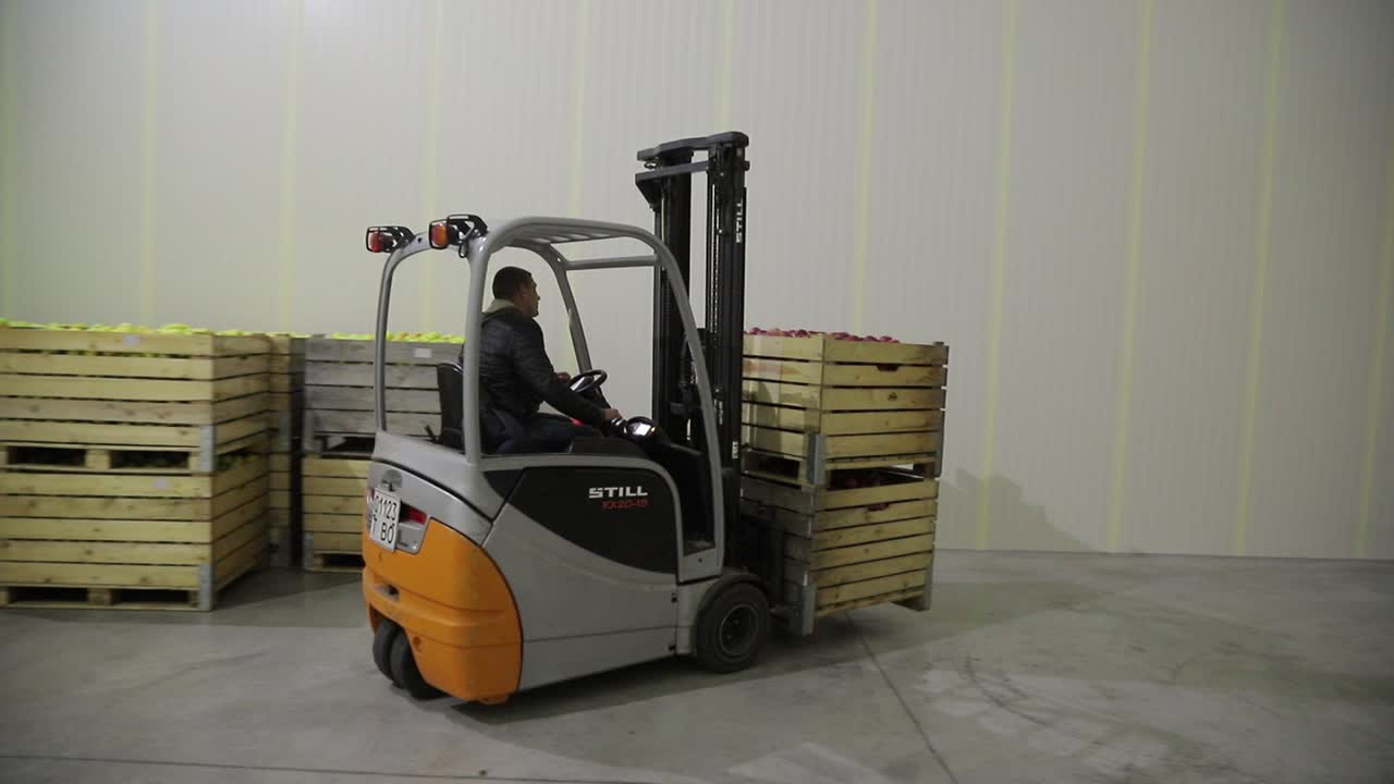 A worker on a loader delivers wooden boxes of ripe apples to the warehouse and places them in rows. Plant for the production of juices.