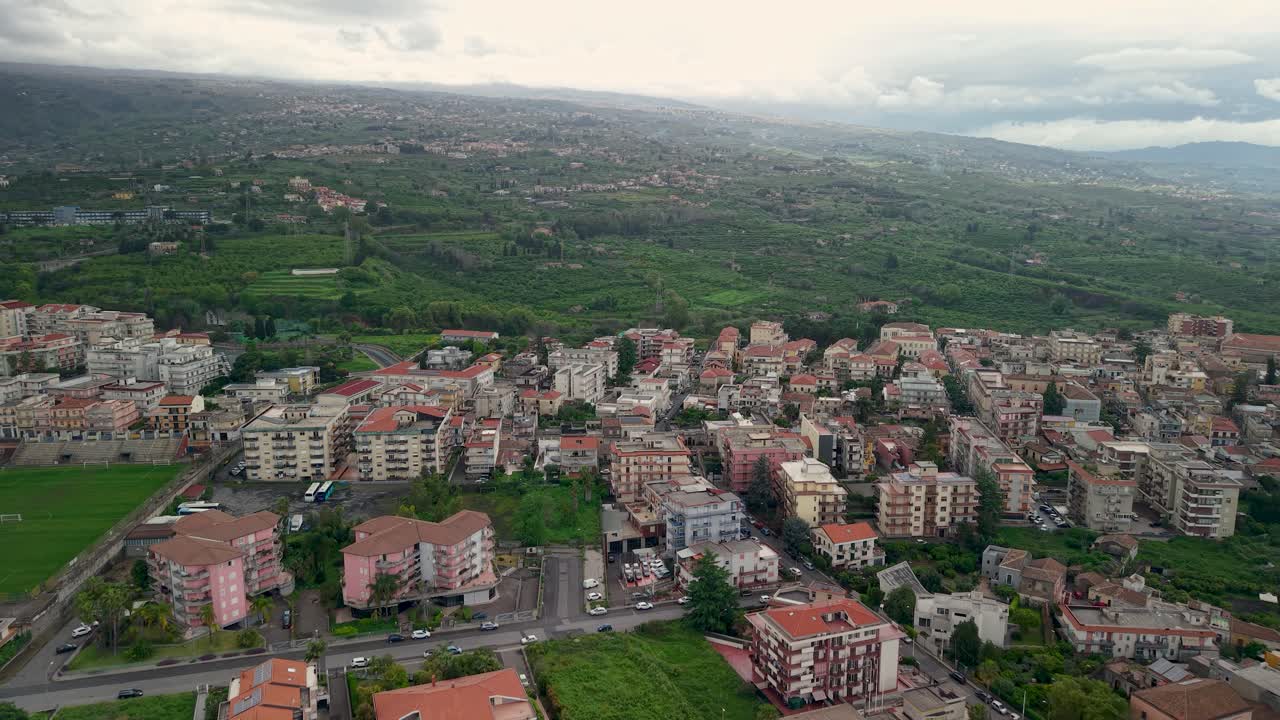 Drone panoramic approach to apartment structures near incomplete stadium complex in Sicily, aging overgrown area