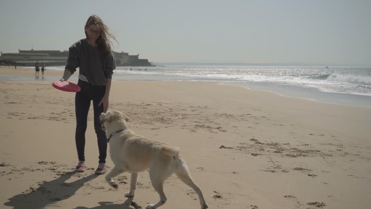 una joven sonriente y un perro jugando con un disco volador rojo.