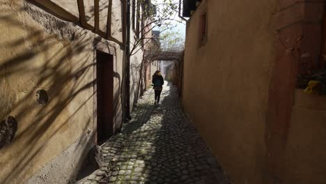 female tourist walking around sunny small street with cobblestone roads and half-timbered houses in kaysersberg, france