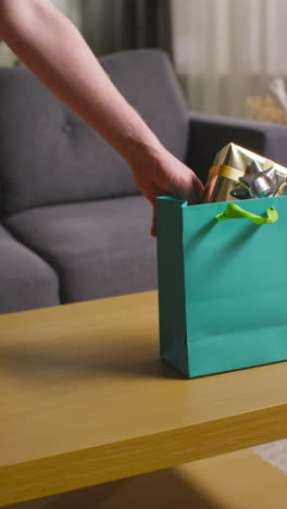 Vertikales-Video-Eines-Mannes,-Der-Verpackte-Geschenke-In-Bunten-Tüten-Mit-Etikett-Auf-Den-Tisch-Im-Wohnzimmer-Zu-Hause-Legt