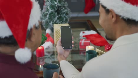 Happy-son-and-father-holding-coffee-mugs-making-christmas-video-call-on-smartphone-with-copy-space