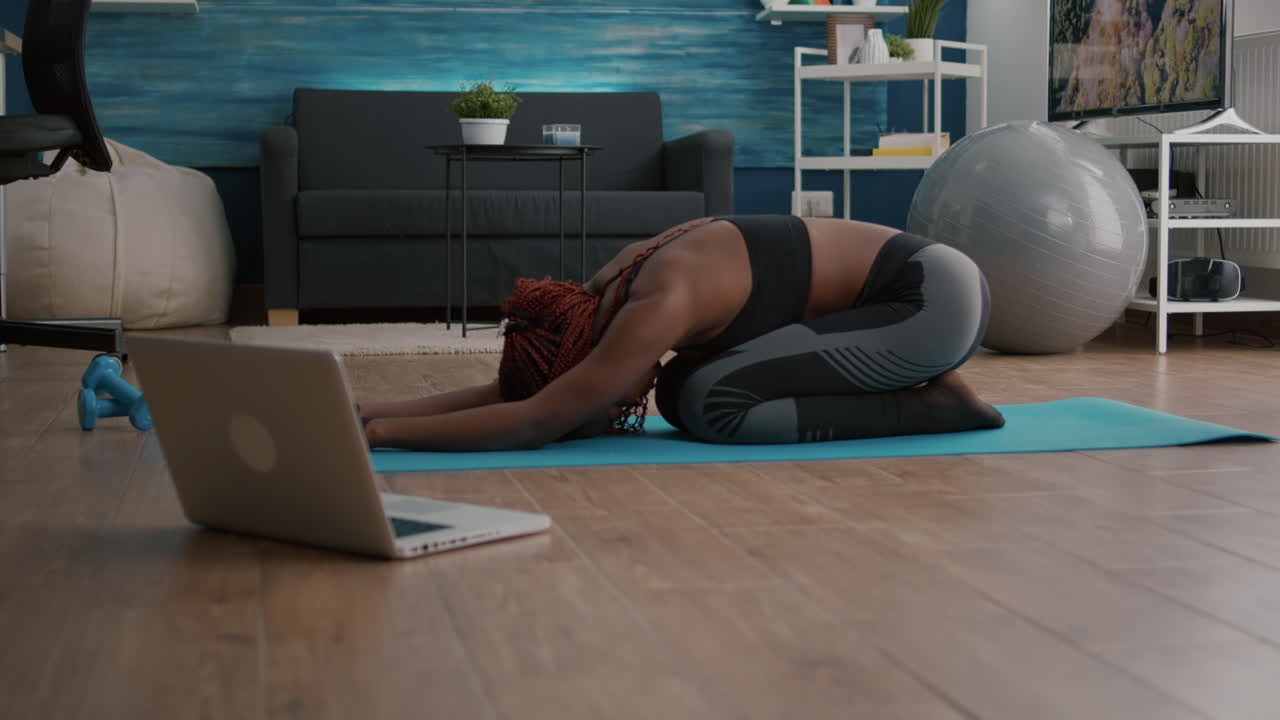 mujer delgada con piel negra sentada en un mapa de yoga haciendo ejercicio físico por la mañana