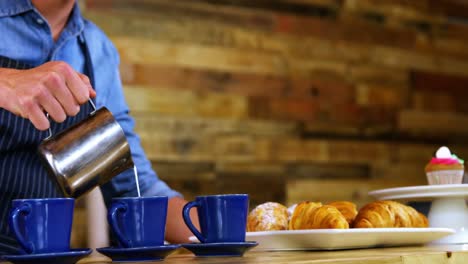 Waiter-pouring-milk-in-coffee-at-counter