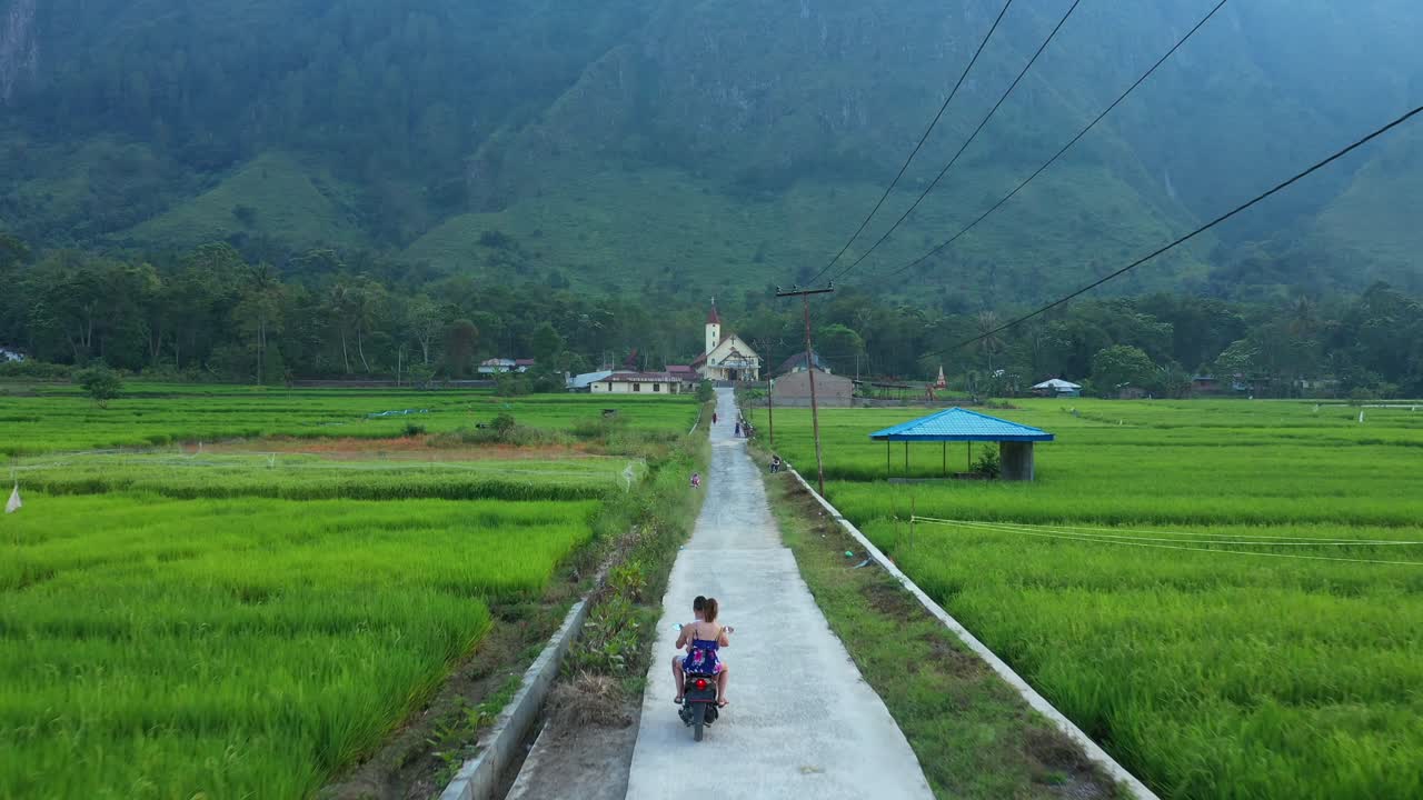 인도네시아 북부 수마트라의 사모시르 섬에 있는 교회로 이어지는 계단식 논 사이의 길에서 스쿠터를 타고 남녀를 따라다니는 드론