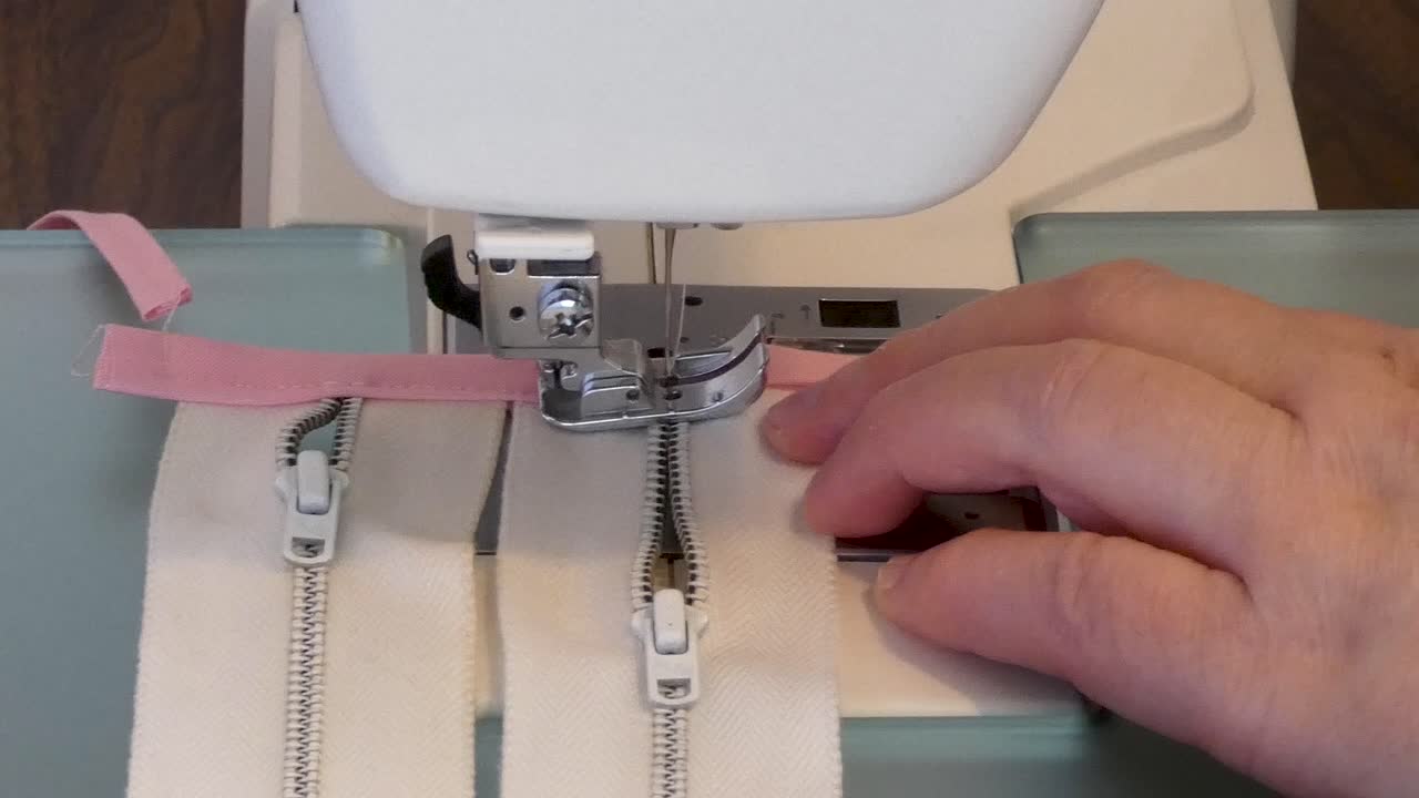 A woman sews fabric stops on tops of metal zippers.