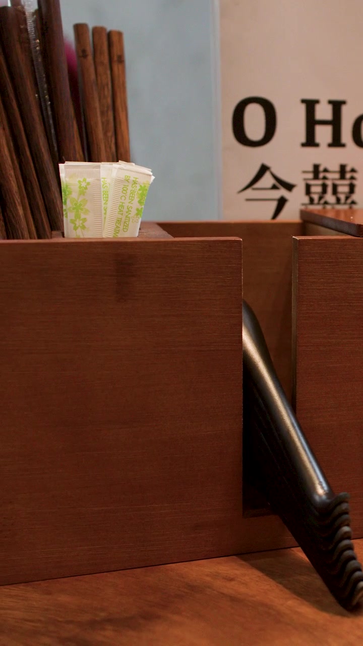 Close-up of a customer hand taking chopsticks and soup spoon from a restaurant wooden dispenser.
