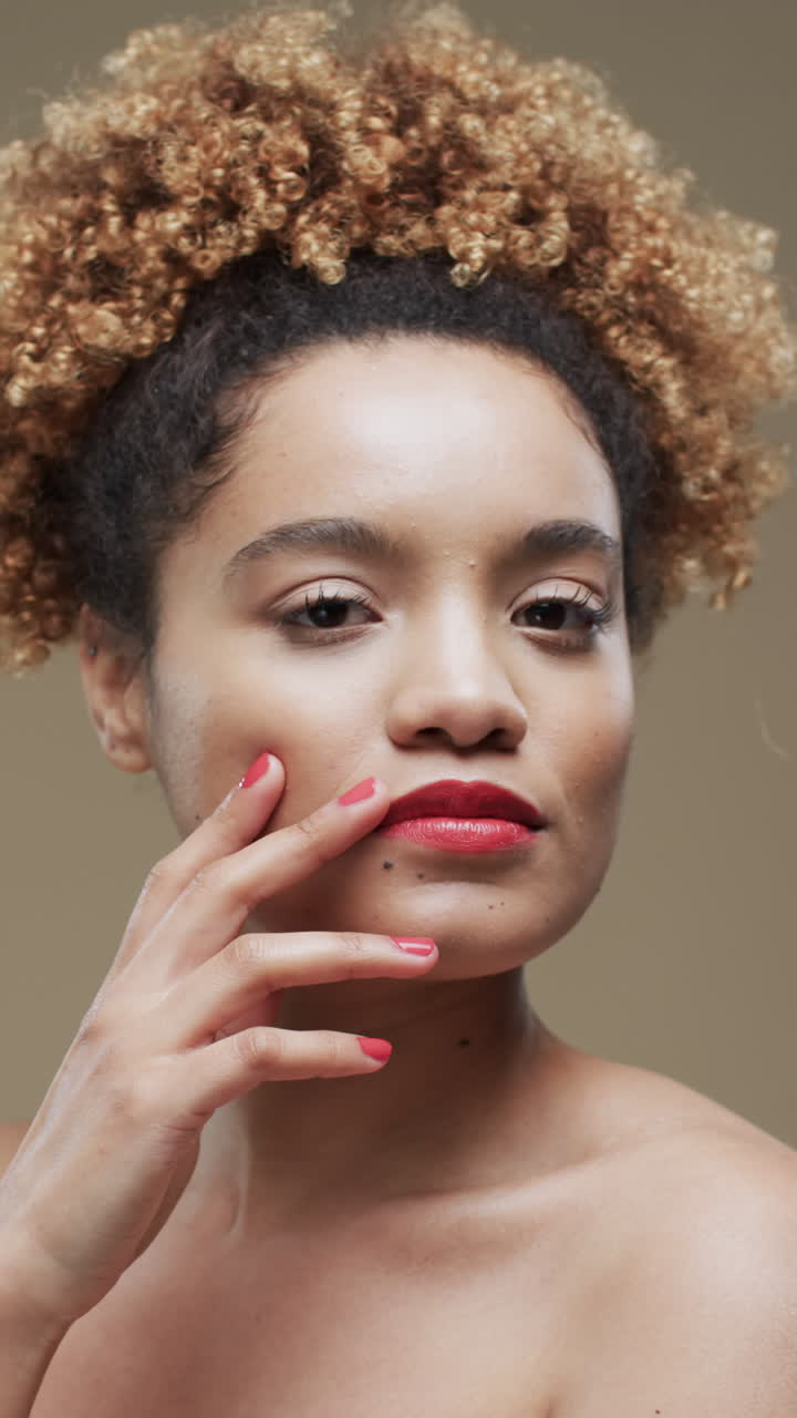 Vertical video of biracial woman with dark hair and red lips on beige background, slow motion