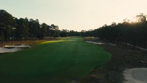 Eine-Drohne-Schoss-über-Das-Fairway-Eines-Golfplatzes,-Als-Die-Aufgehende-Sonne-über-Den-Bäumen-Gipfelte