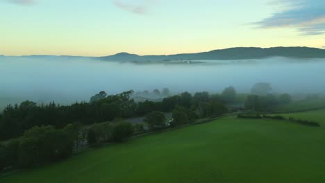 flying over green fields and m6 motorway towards mist and fog bank and distant hills and mountains at dawn
