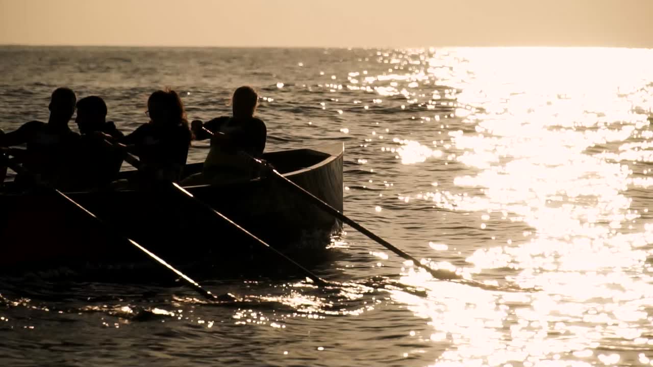 일몰이나 일출에 배를 타고 함께 노를 젓는 의욕적인 사람들의 실루엣