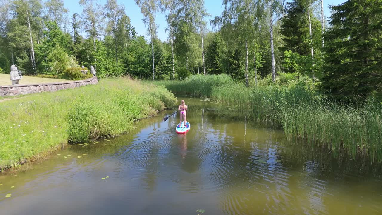 Ujęcie z lotu ptaka młodej kobiety wiosłującej na stojąco na desce SUP na stawie latem