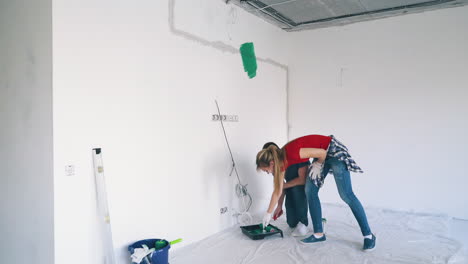 woman-with-man-takes-green-paint-from-plastic-tray-in-room