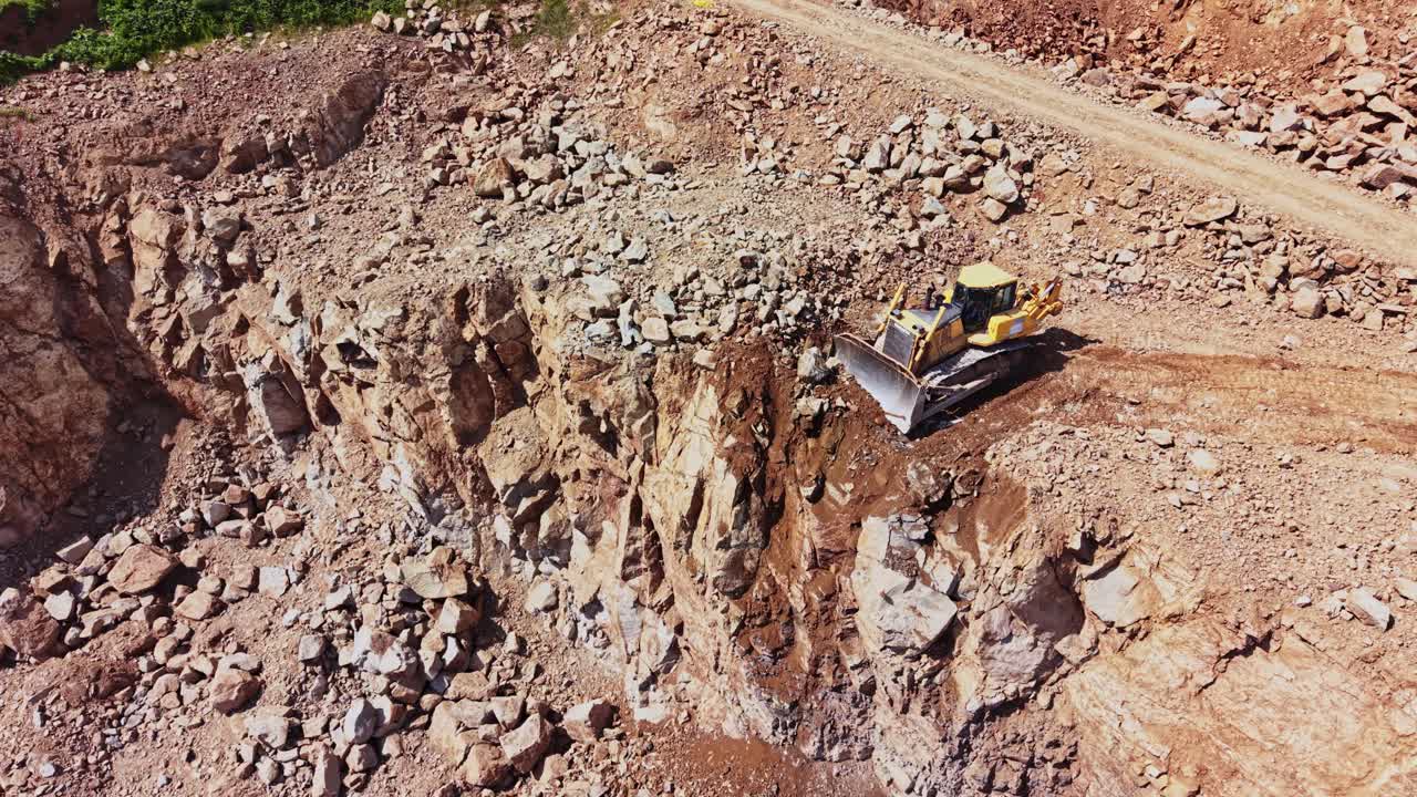 Una excavadora trabaja en terreno rocoso en una obra durante el día.
