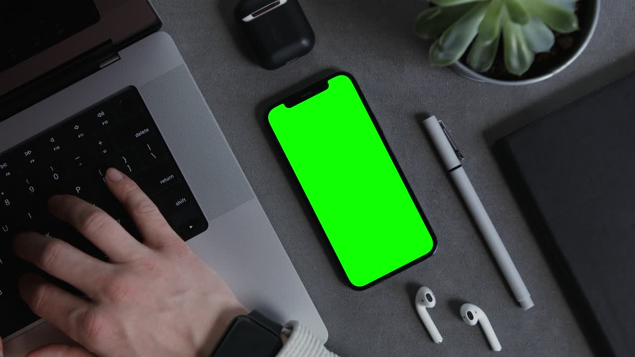 Persona che lavora al laptop con telefono a schermo verde e accessori