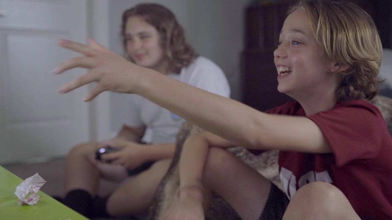 Two teen boys playing video games and laughing at the screen in bedroom
