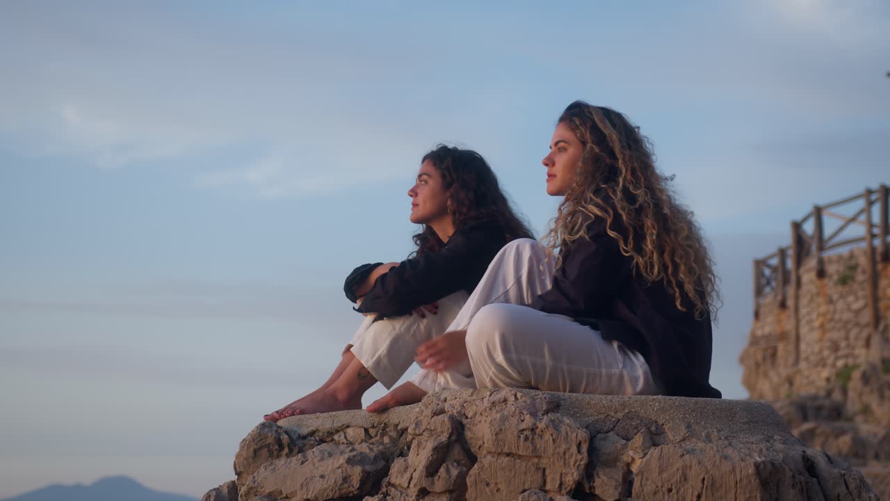 Static shot of two sisters watching the sunset from the rocks in Anacapri, Capri Island, Italy