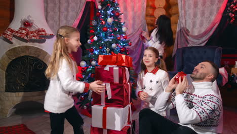 happy new year celebration at home. father and his daughters playing with toys near christmas presents. mom is decorating christmas tree.