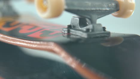 a creative macro detailed shot of a mini skateboard, tiny white wheels, upside down fingerboard on a 360 rotating stand, shiny mirror reflection, professional lighting, cinematic 4k video tilt up